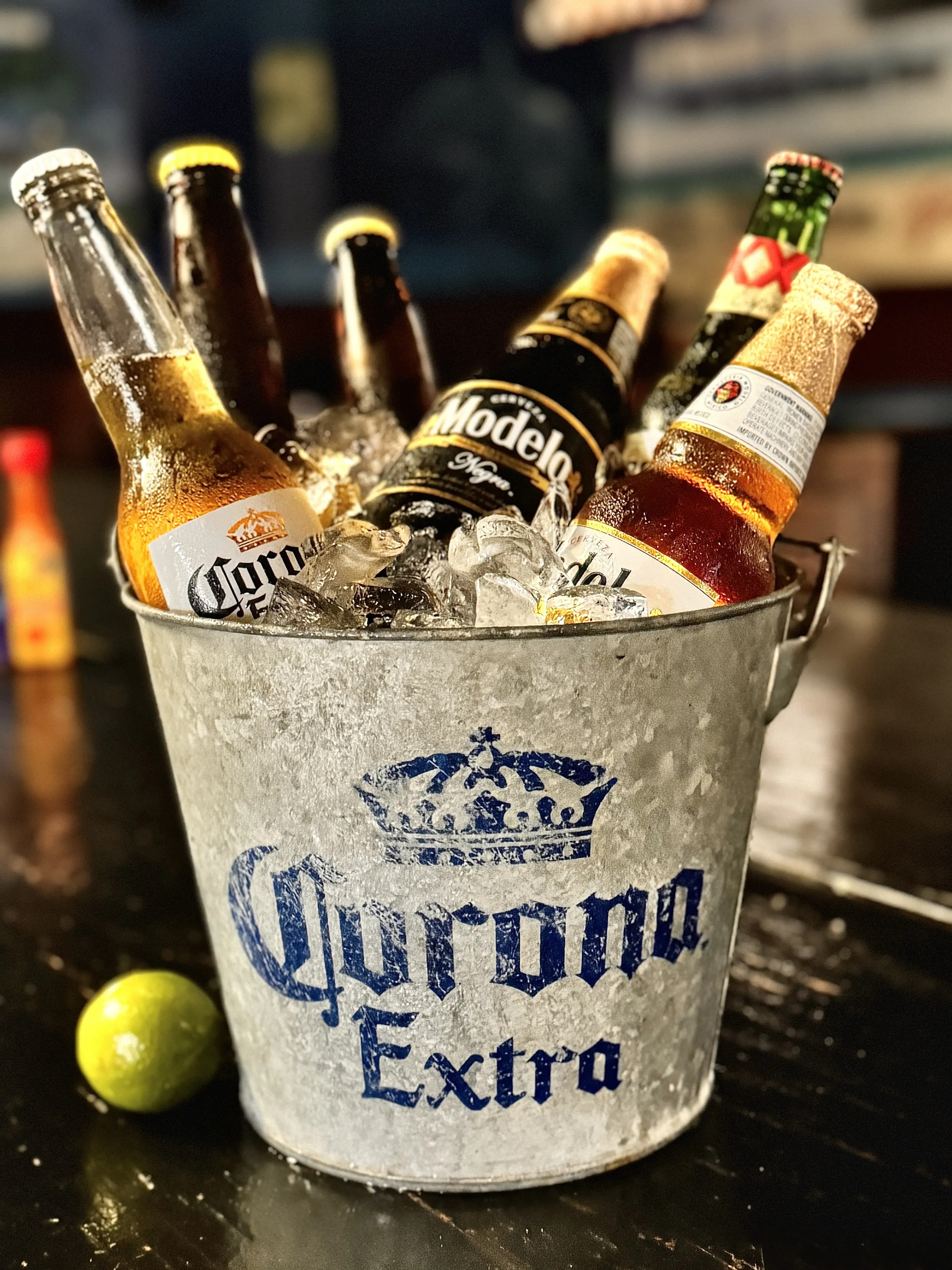 Silver beer bucket overflowing with ice and seating beers including corona, modelo, dos equis, victoria, and other Mexican beers.