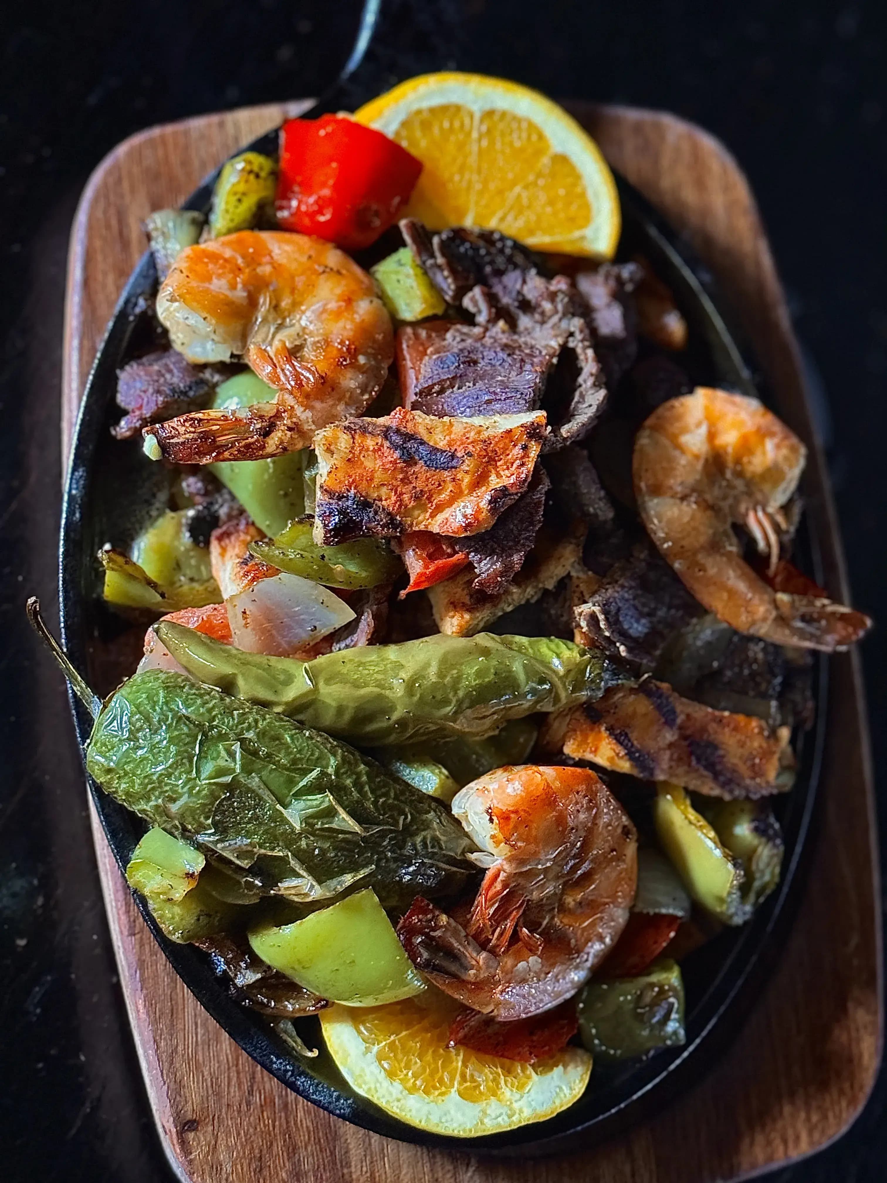 Steaming Hot Fajitas with large shrimp served on cast-iron which is also seated on a thick wooden tray.