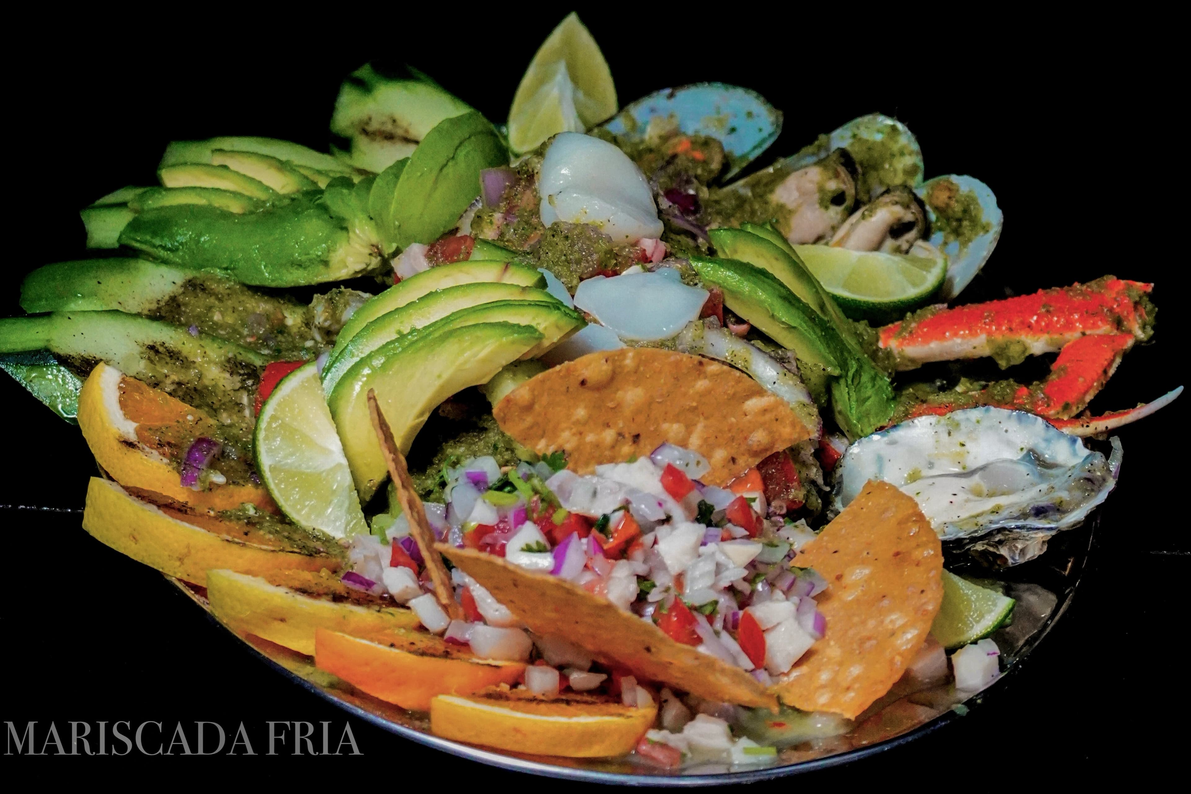 A large plate stuffed with ceviche,crab,oysters, muscles, scalops avocado, lime, cucumbers and orage sclices. Mexican seafood dish called Mariscada.